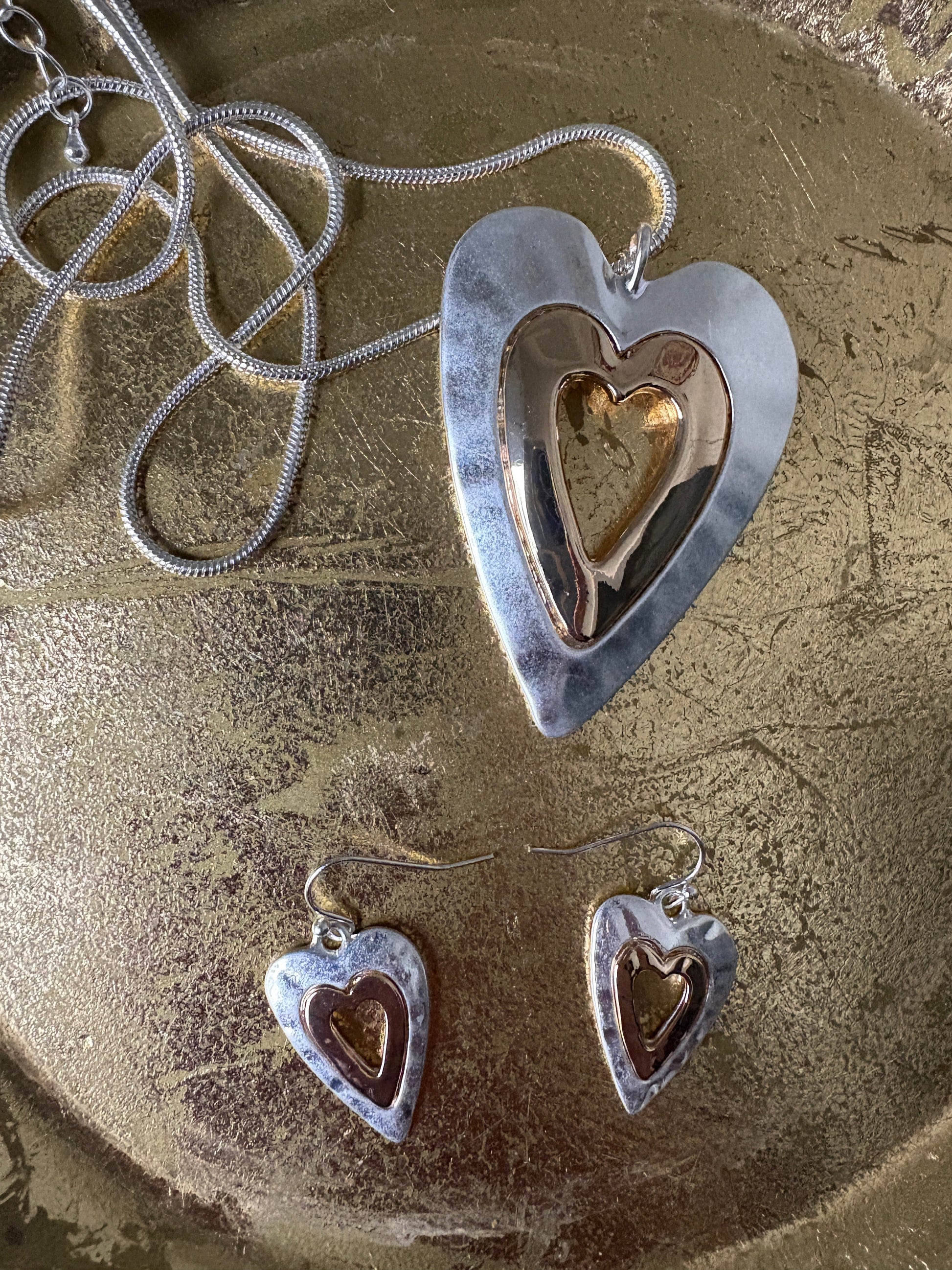 Heart-shaped silver pendant with a gold interior on a textured surface